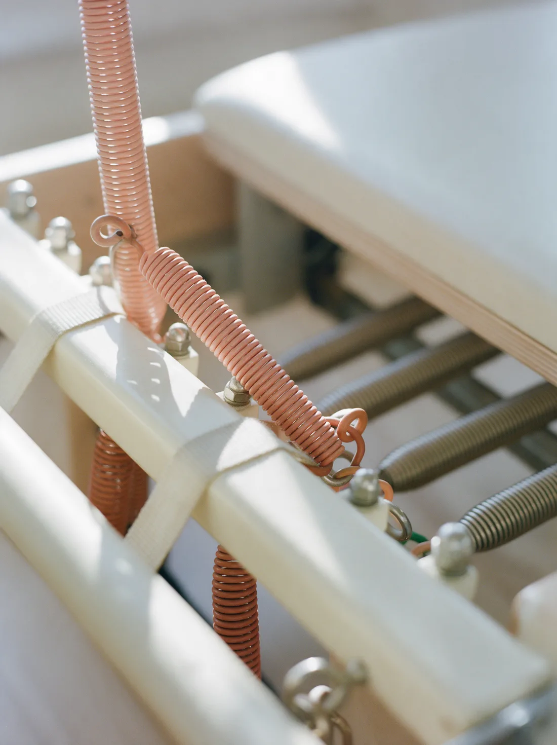 Detail van de koraalkleurige veren van een pilatesreformer in zacht ochtendlicht.